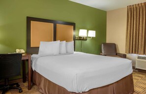 Ein Hotelzimmer mit einem großen Bett, einem Schreibtisch mit Telefon, einem Sessel und einer Wandlampe.