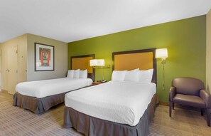 A hotel room with two beds, a chair, and a framed picture on the wall.