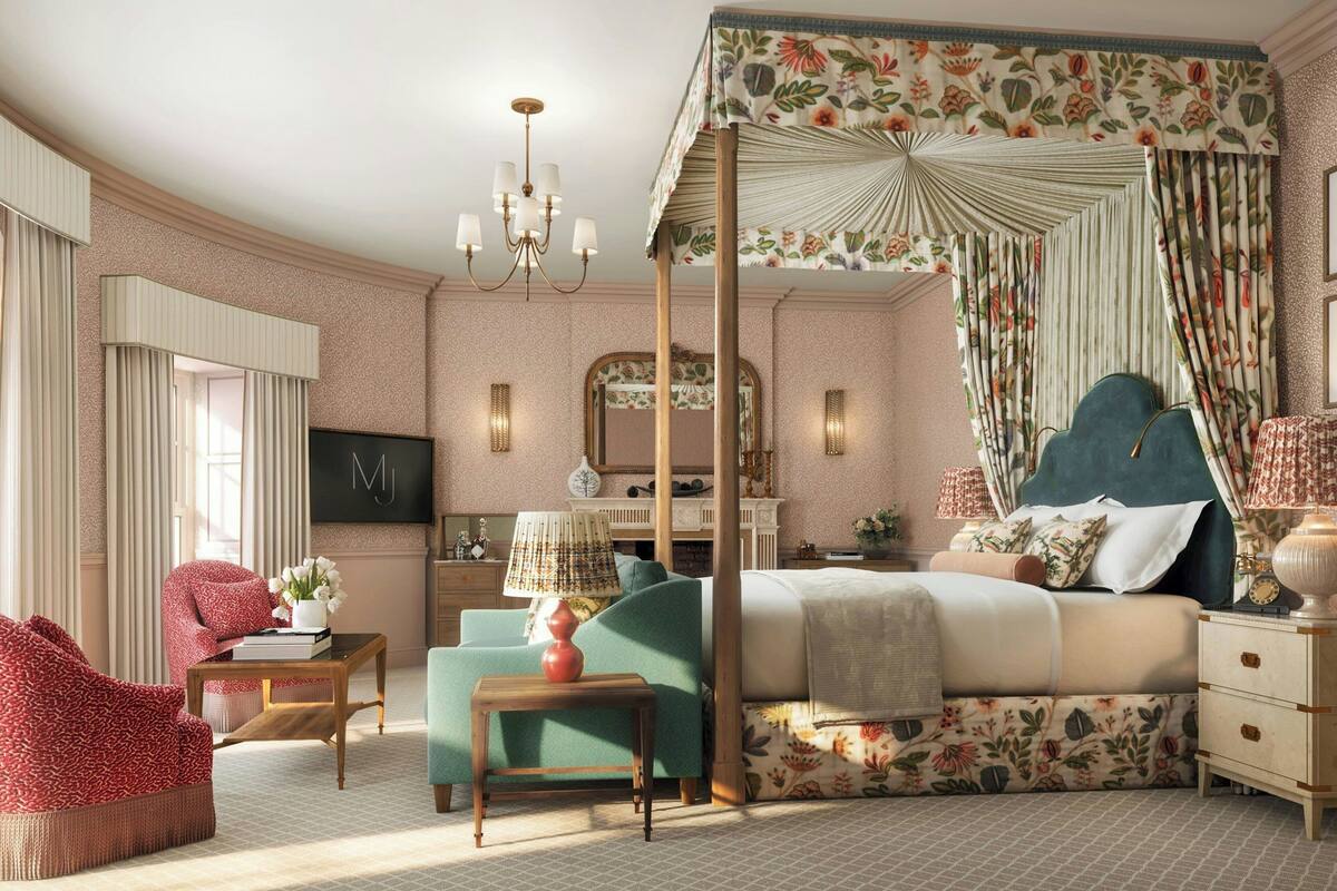 A bedroom with a canopy bed, a sitting area with a chair and a table, and a television on the wall.