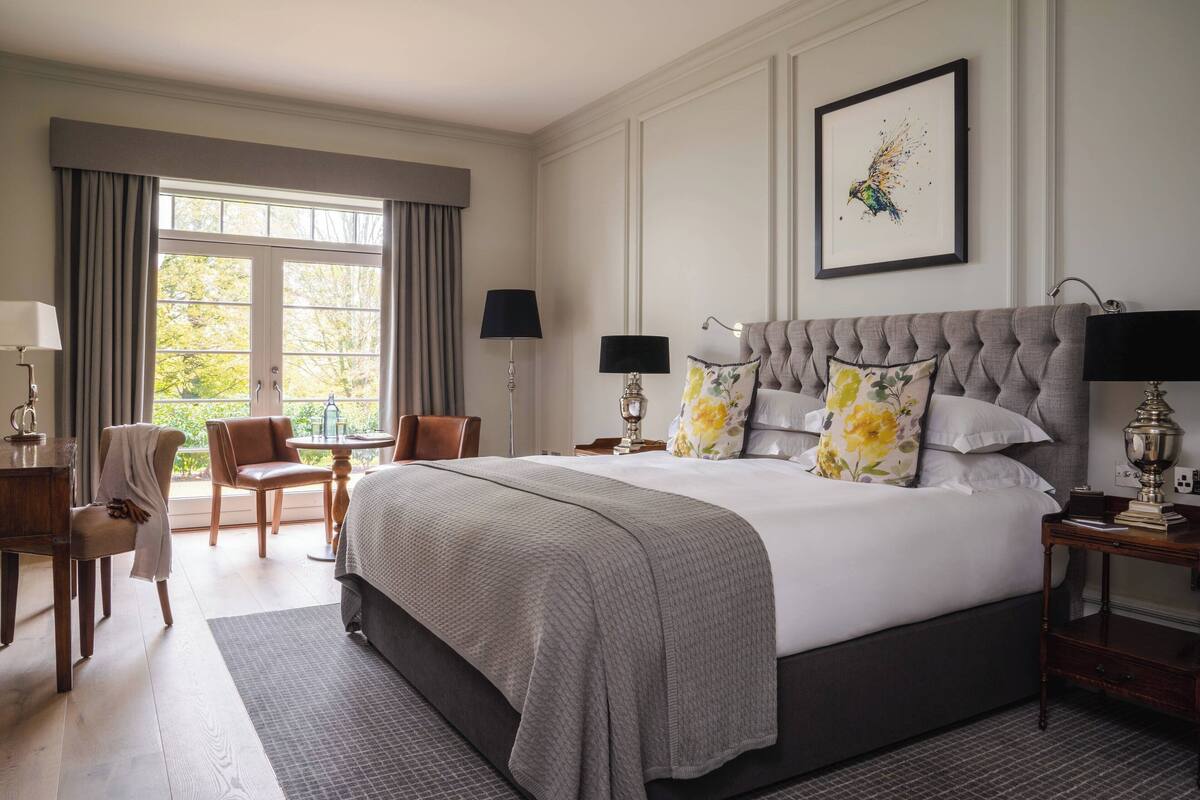 A spacious bedroom with a large bed, a sitting area with a chair and table, and a view through a large window.