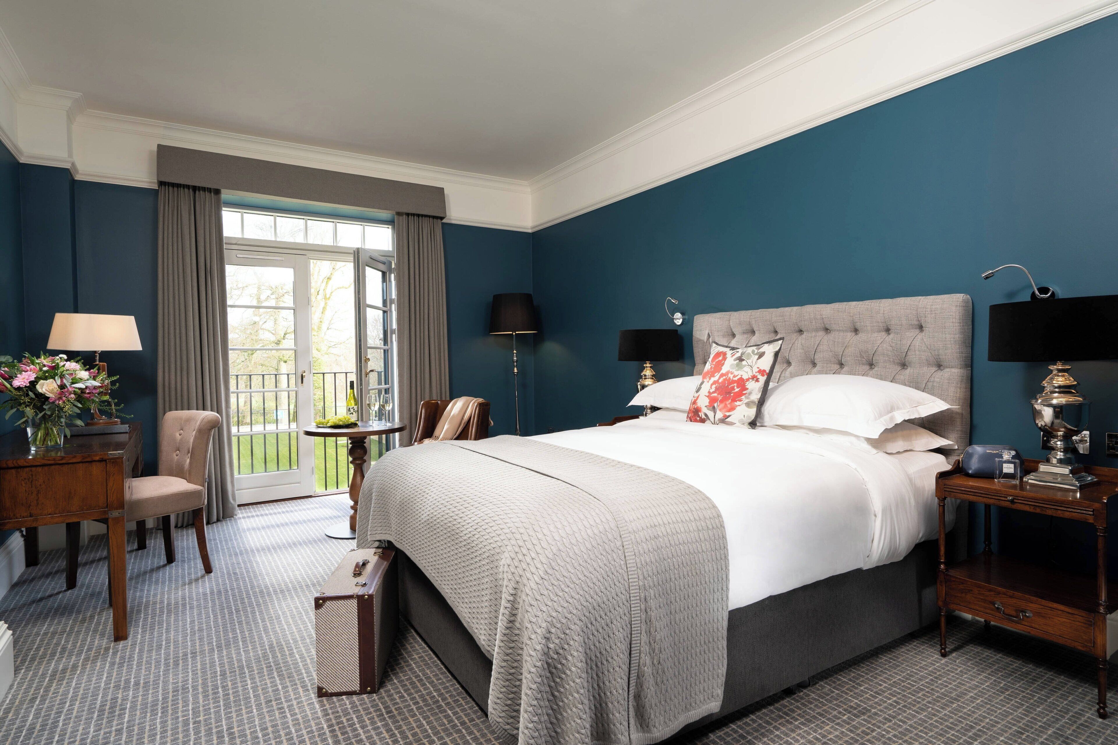 A hotel room with a large bed, a desk, a chair, a small table, and a window with curtains.