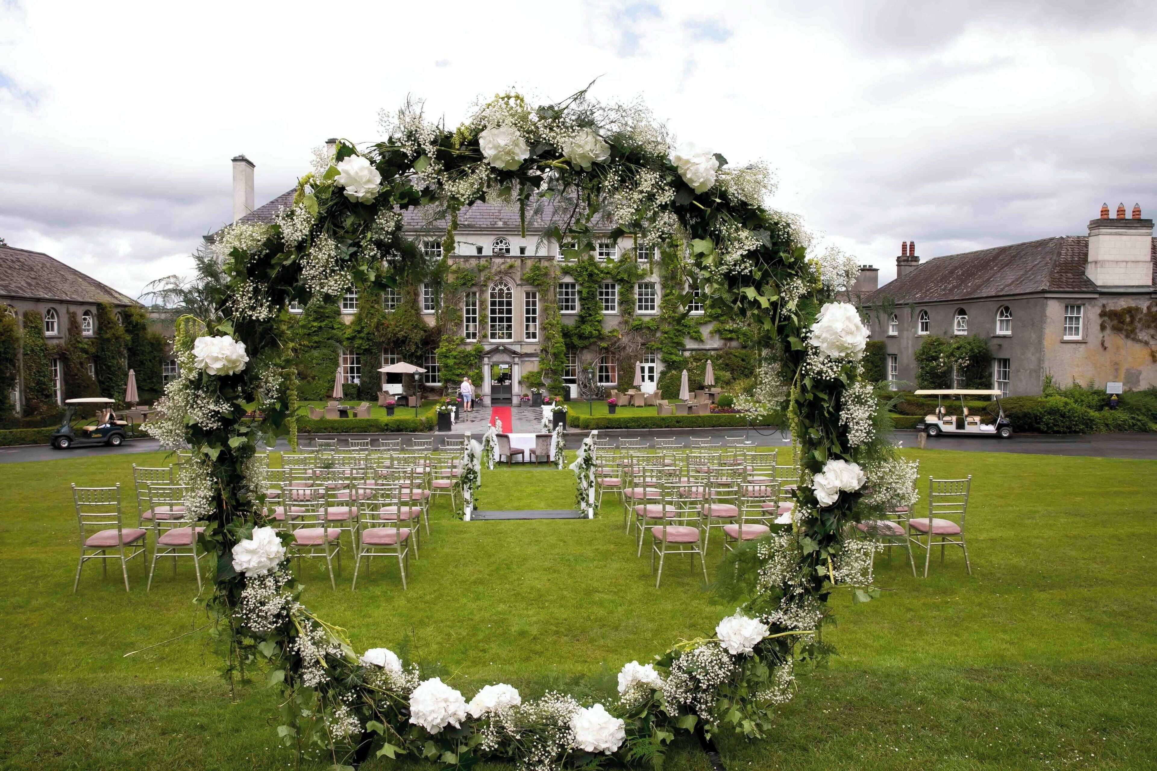 An outdoor wedding ceremony setup with a heart-shaped floral arch and rows of chairs on a lawn.