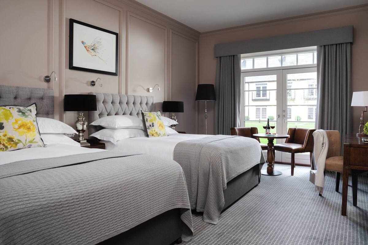 A hotel room with two beds, a sitting area with a table and chairs, and a large window with curtains.