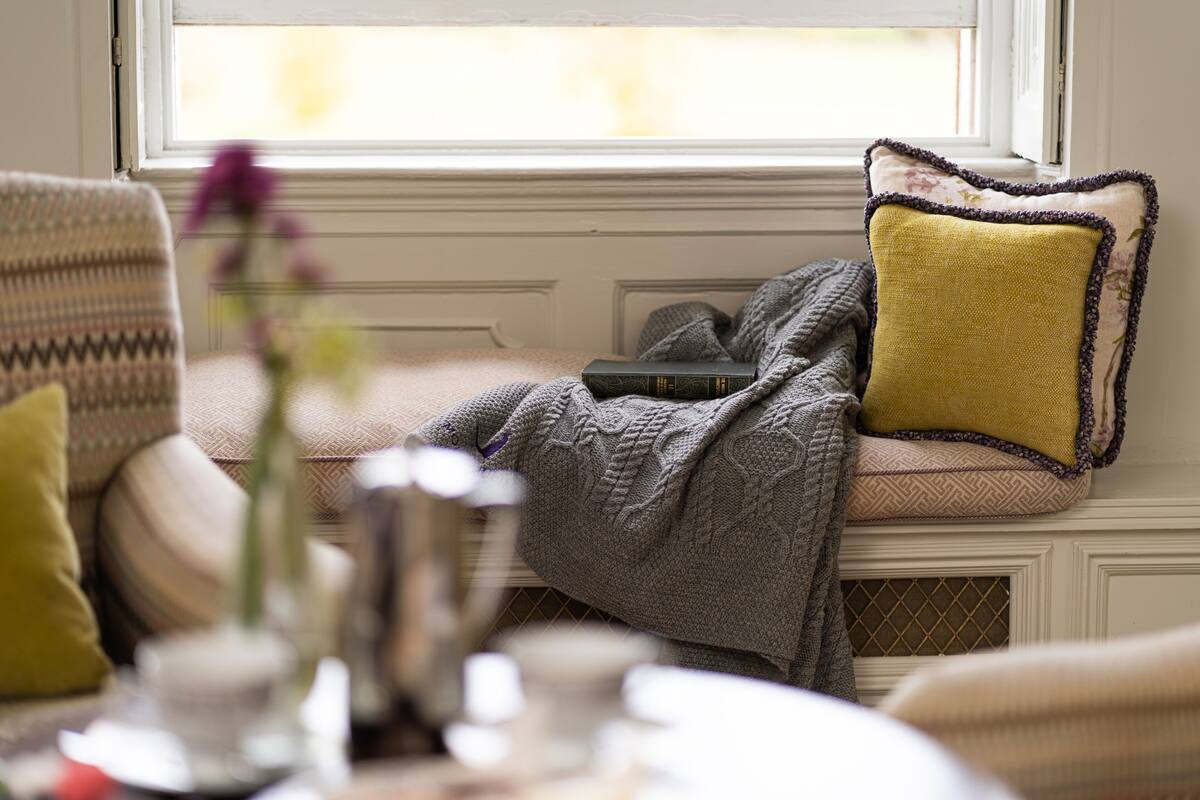 A cozy seating area with a cushioned bench, a small table with a vase, and a window with a view.