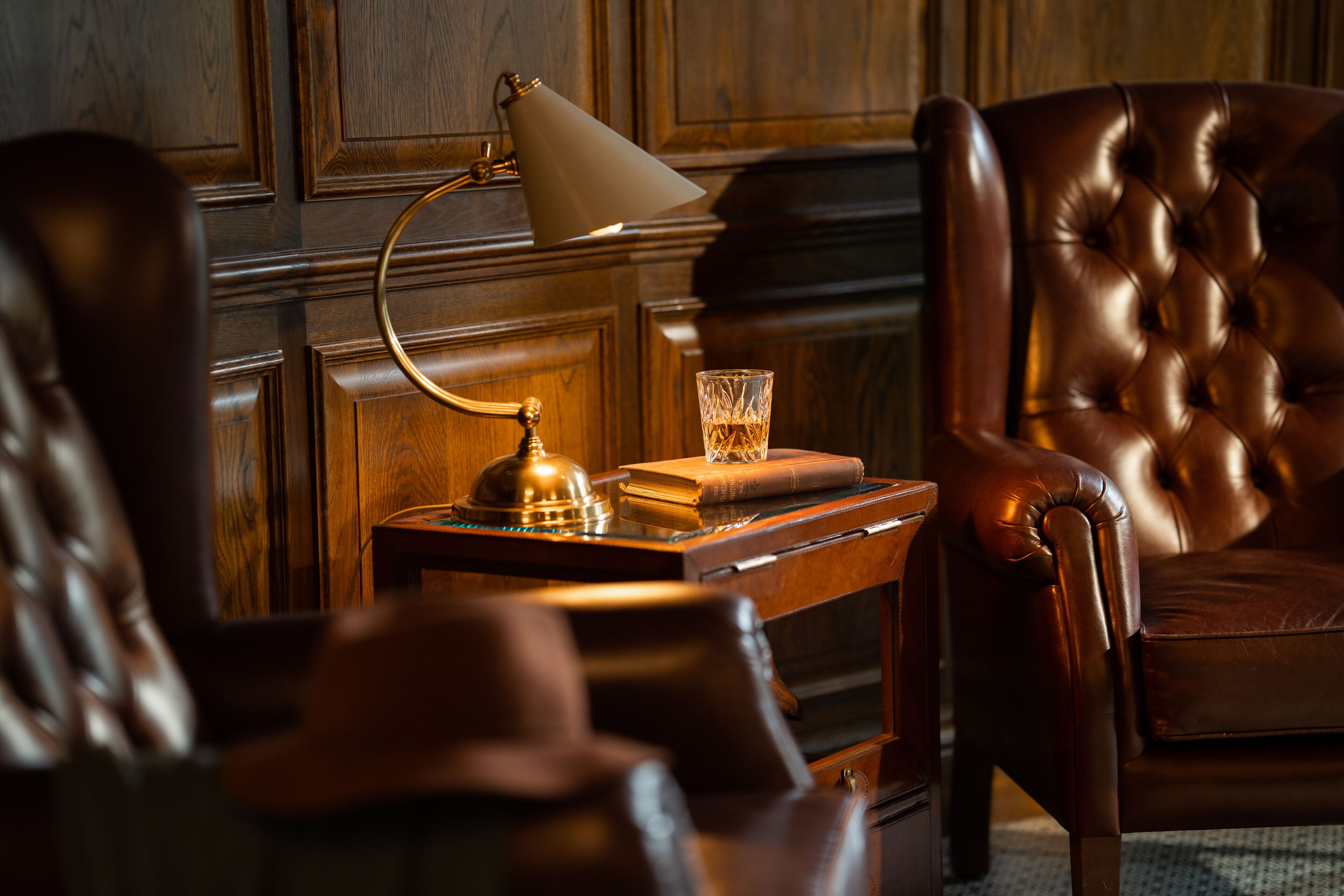 A leather armchair, a wooden side table with a lamp, and a glass of water on the table.