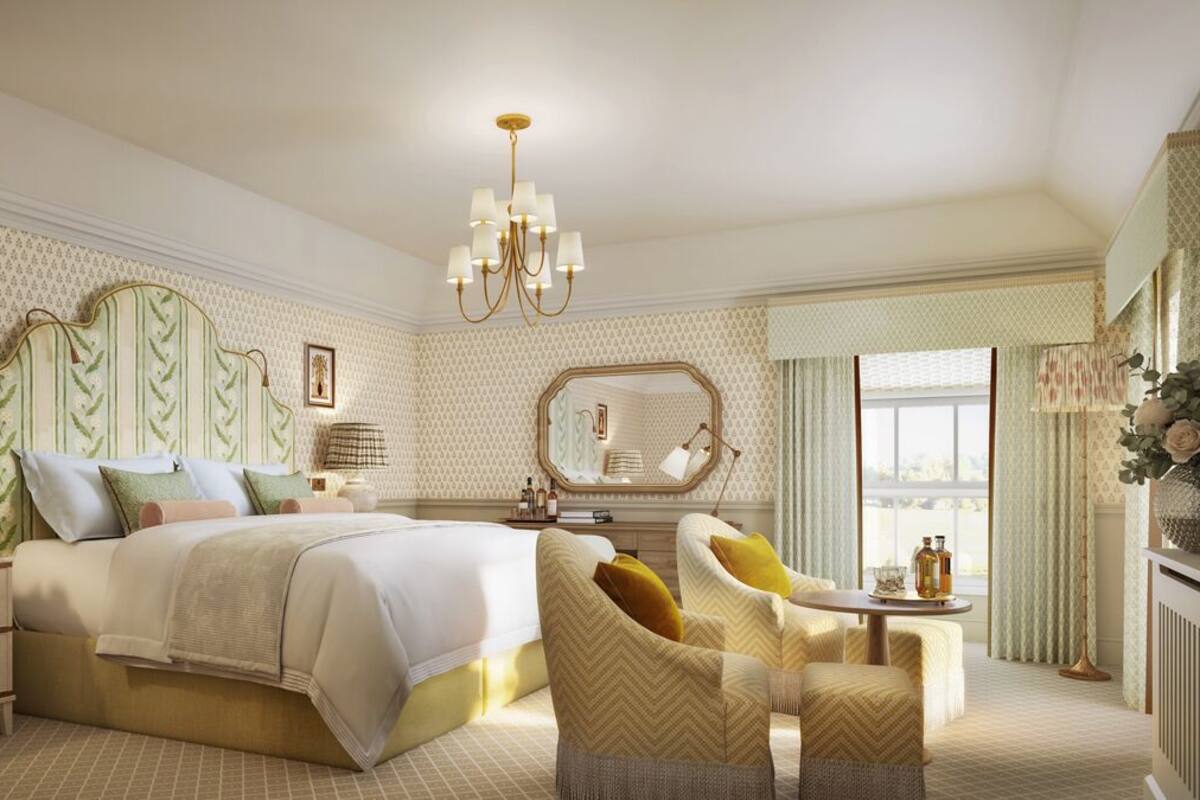 A bedroom with a large bed, a bedside table, a chair, a mirror, and a chandelier.