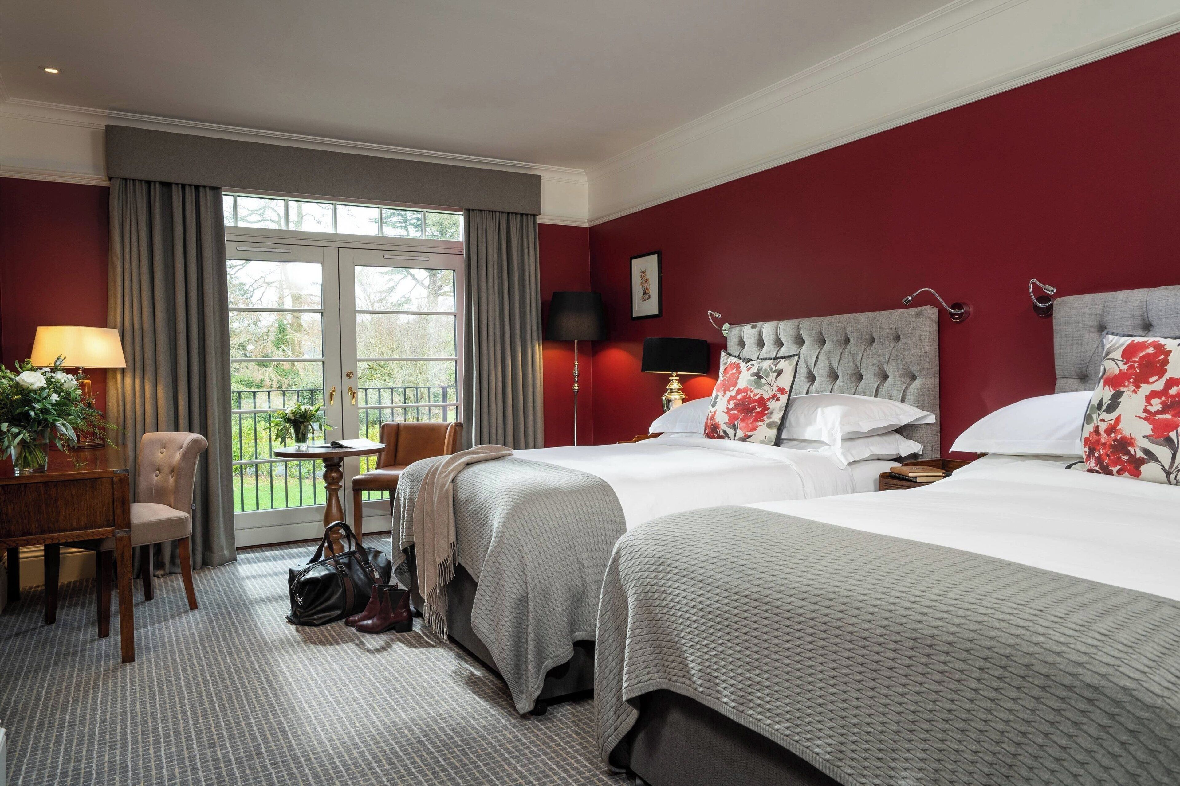 A hotel room with two beds, a desk, a chair, and a view of the outdoors.