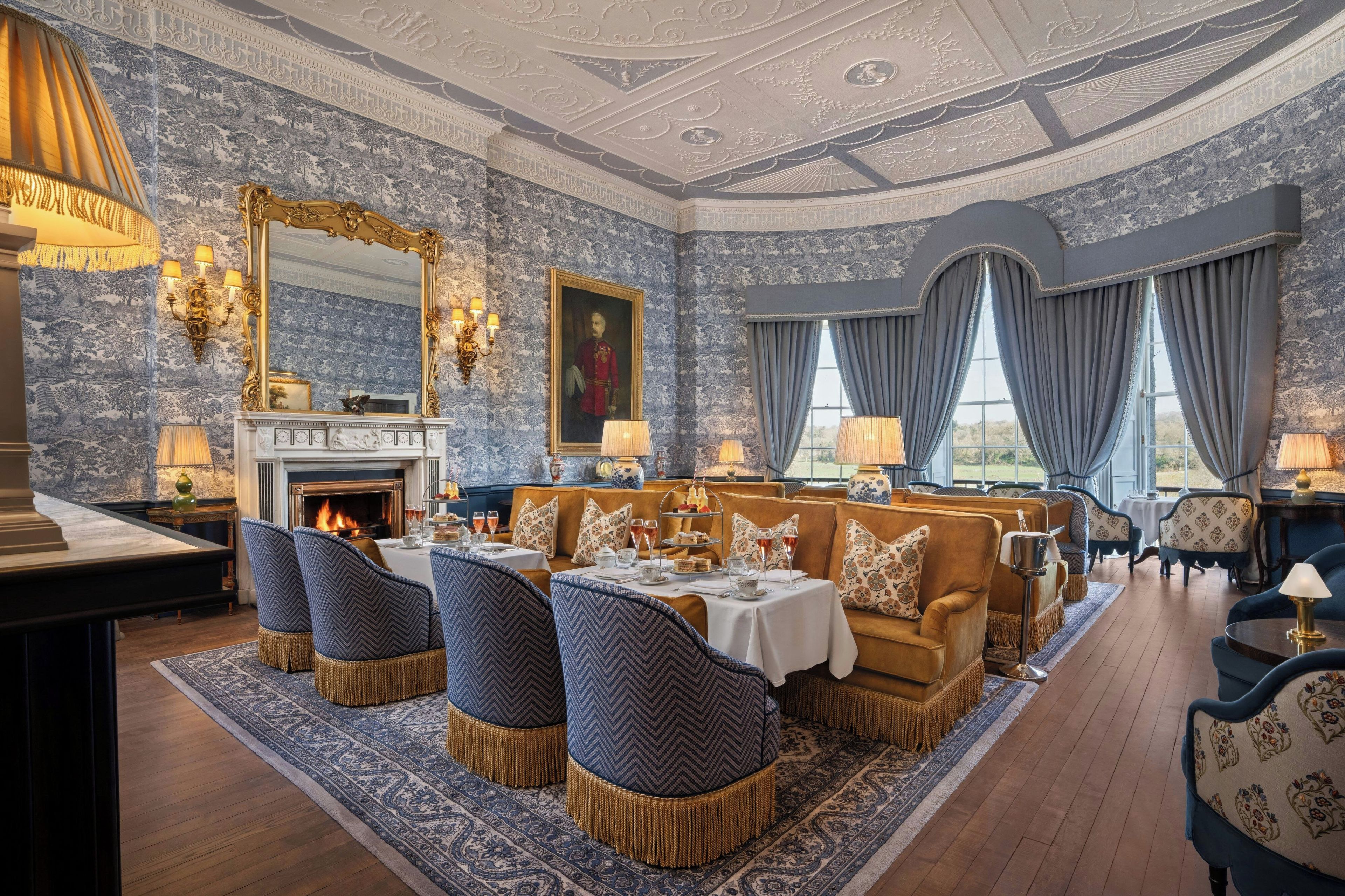 A luxurious room with a fireplace, ornate ceiling, and a dining area with a table set for four.