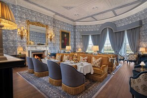 A luxurious room with a fireplace, ornate ceiling, and a dining area with a table set for four.