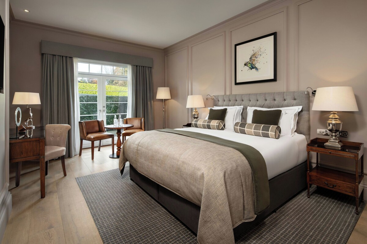 A hotel room with a large bed, two bedside tables, a chair, a desk, and a window with curtains.
