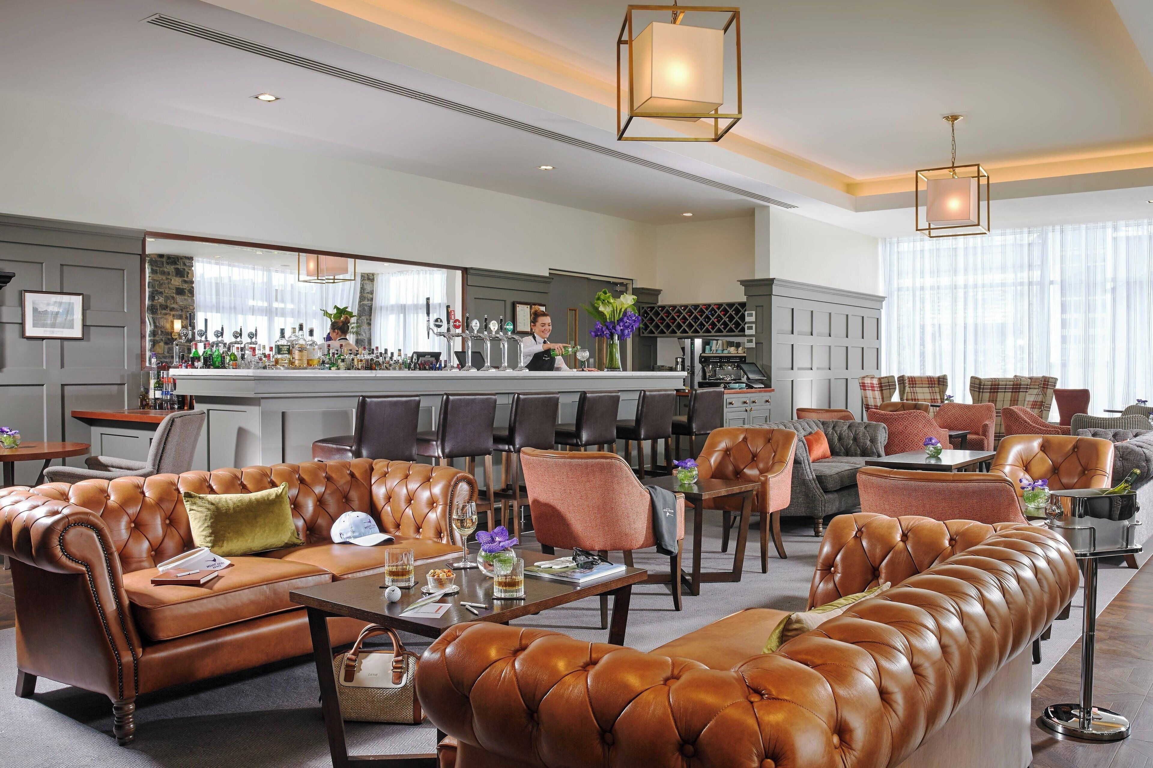 A spacious lounge area with leather sofas, a bar, and a seating area with tables and chairs.
