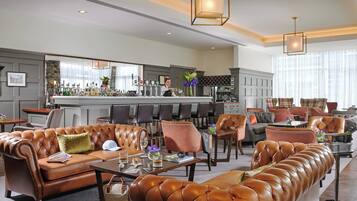 A spacious lounge area with leather sofas, a bar, and a seating area with tables and chairs.