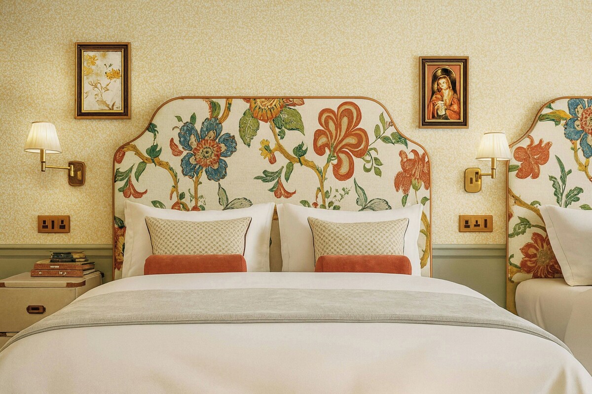 A hotel room with a floral headboard, two bedside tables with lamps, and a bed with pillows.