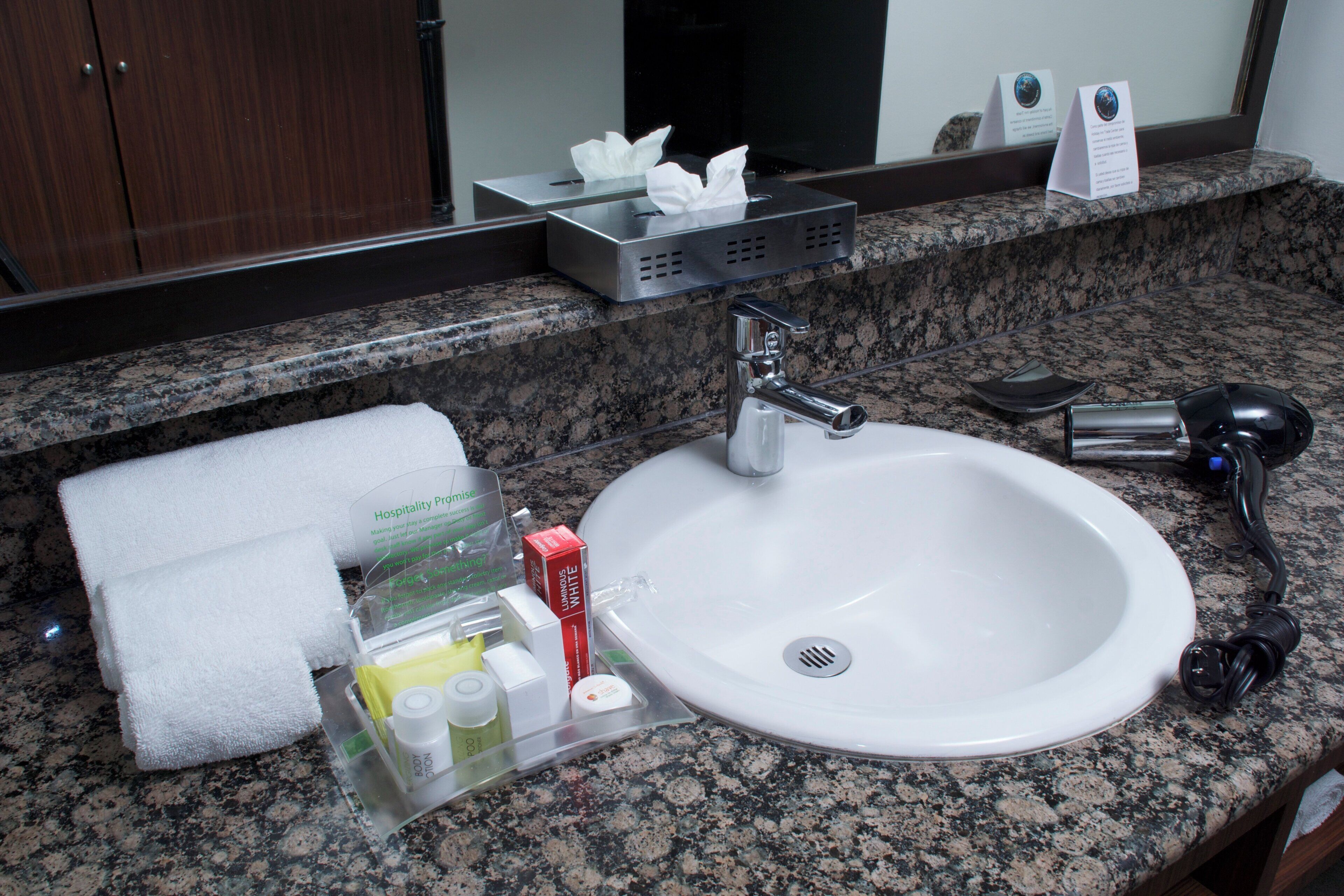 A hotel bathroom with a white sink, a towel, toiletries, and a mirror.
