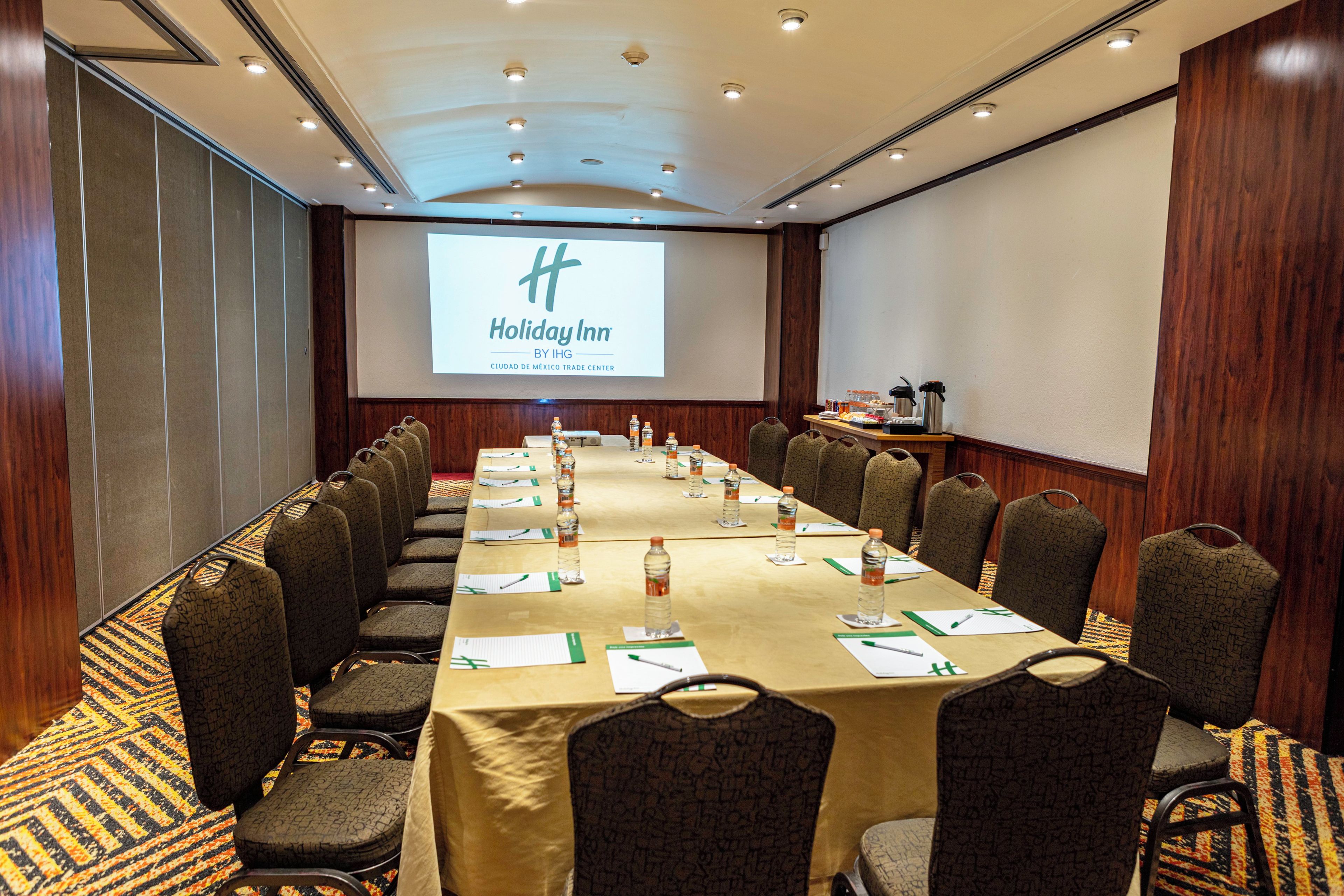 A conference room with a long table, chairs, a projector screen, and a presentation on the screen.