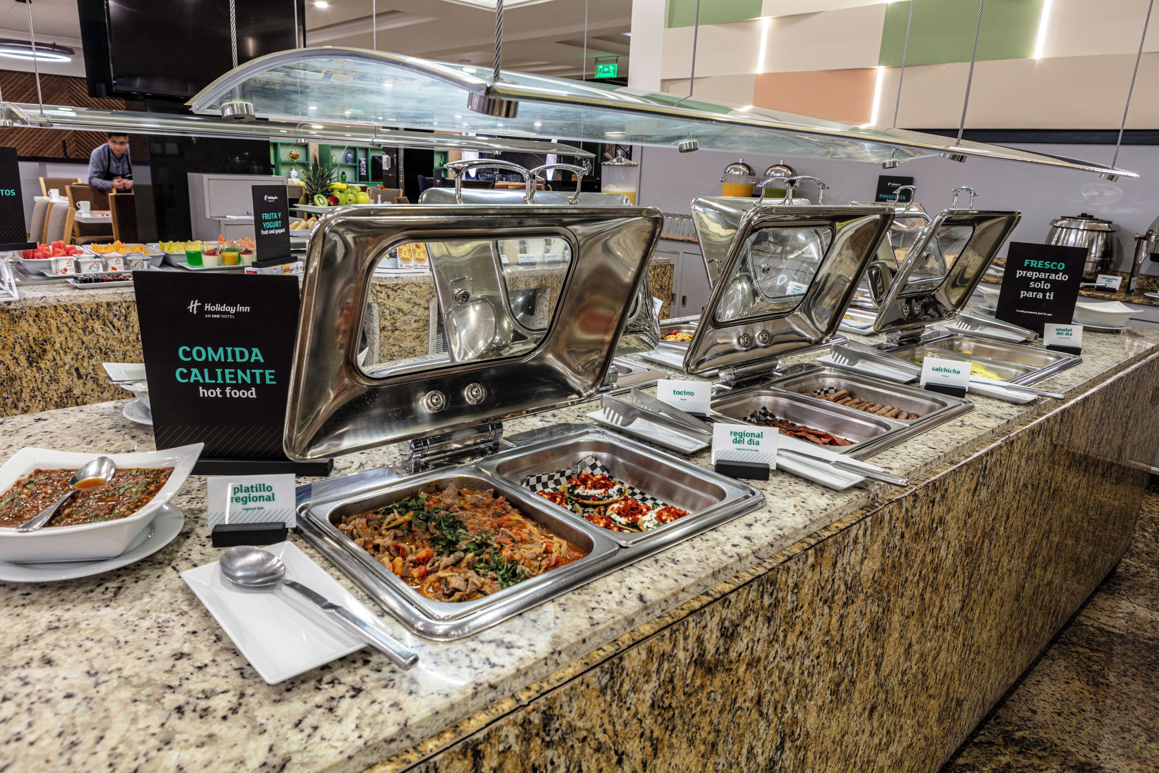 A buffet counter with multiple food stations labeled 'COMIDA CALIENTE' and 'FRESCO preparado solo para ti'.