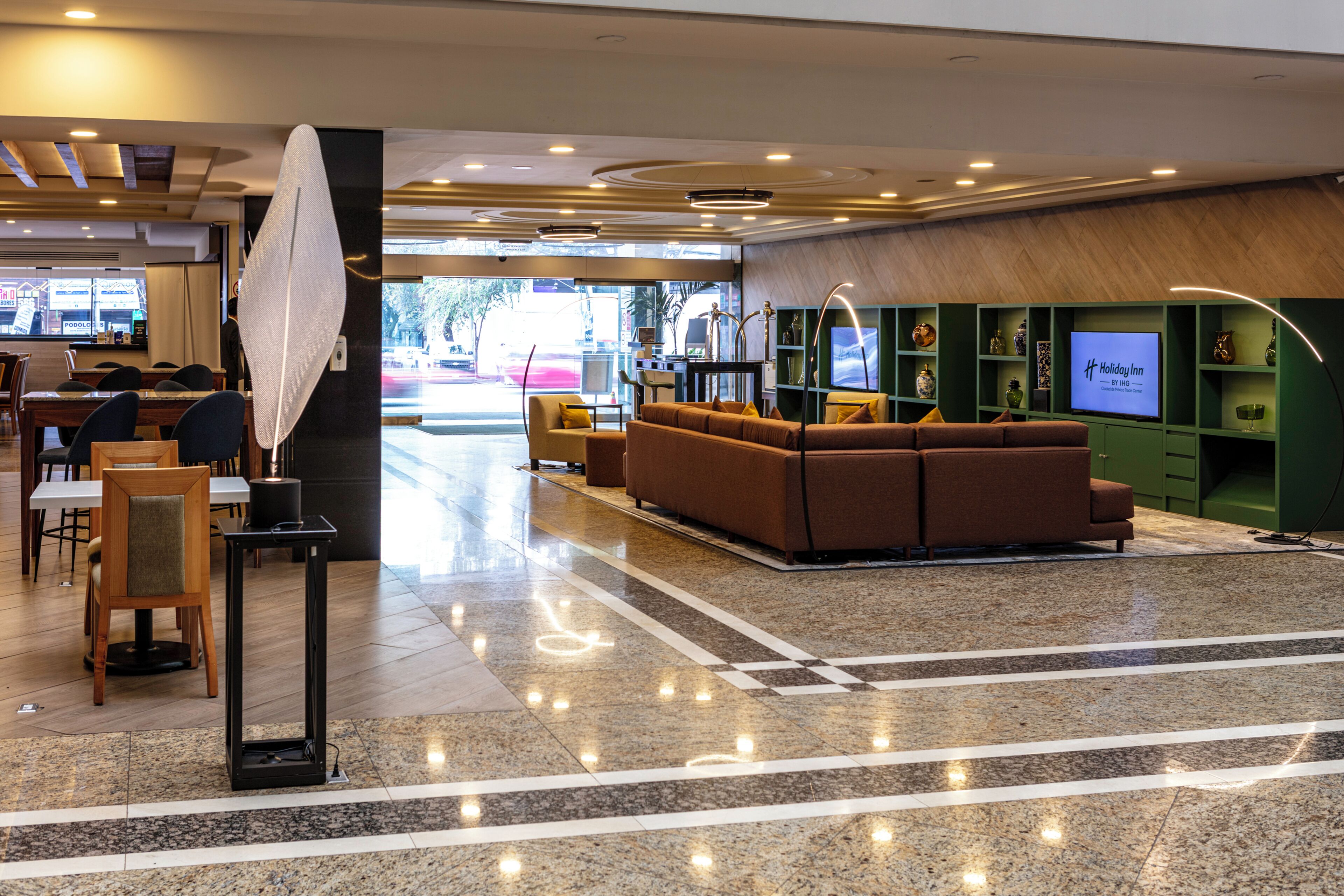 Un hall d’hôtel comprenant un comptoir d’accueil, un espace salon et un téléviseur diffusant des images de l’enseigne « Holiday Inn ».