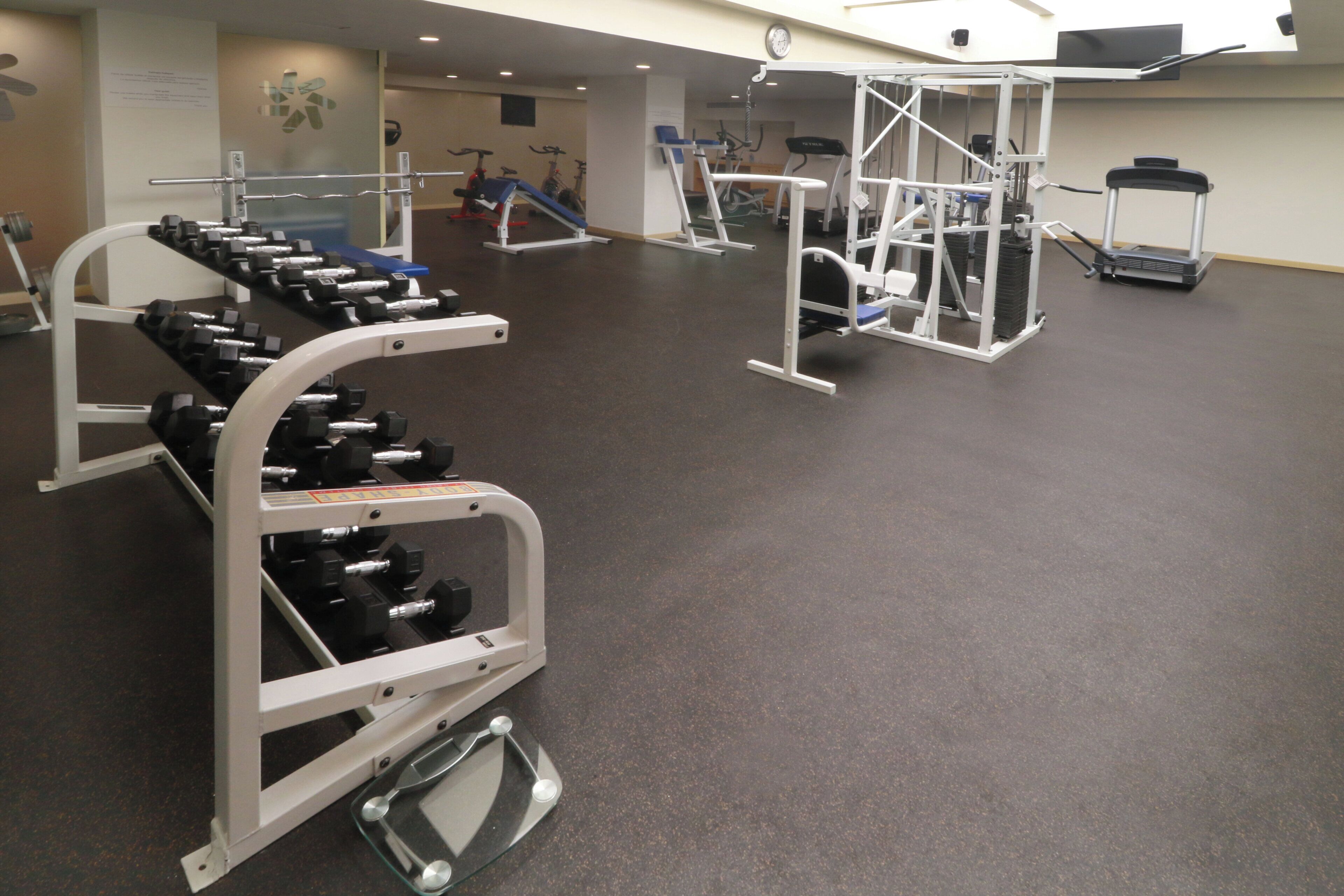 Et fitnesscenter med forskellig træningsudstyr, herunder håndvægte, løbebånd og styrkemaskiner.