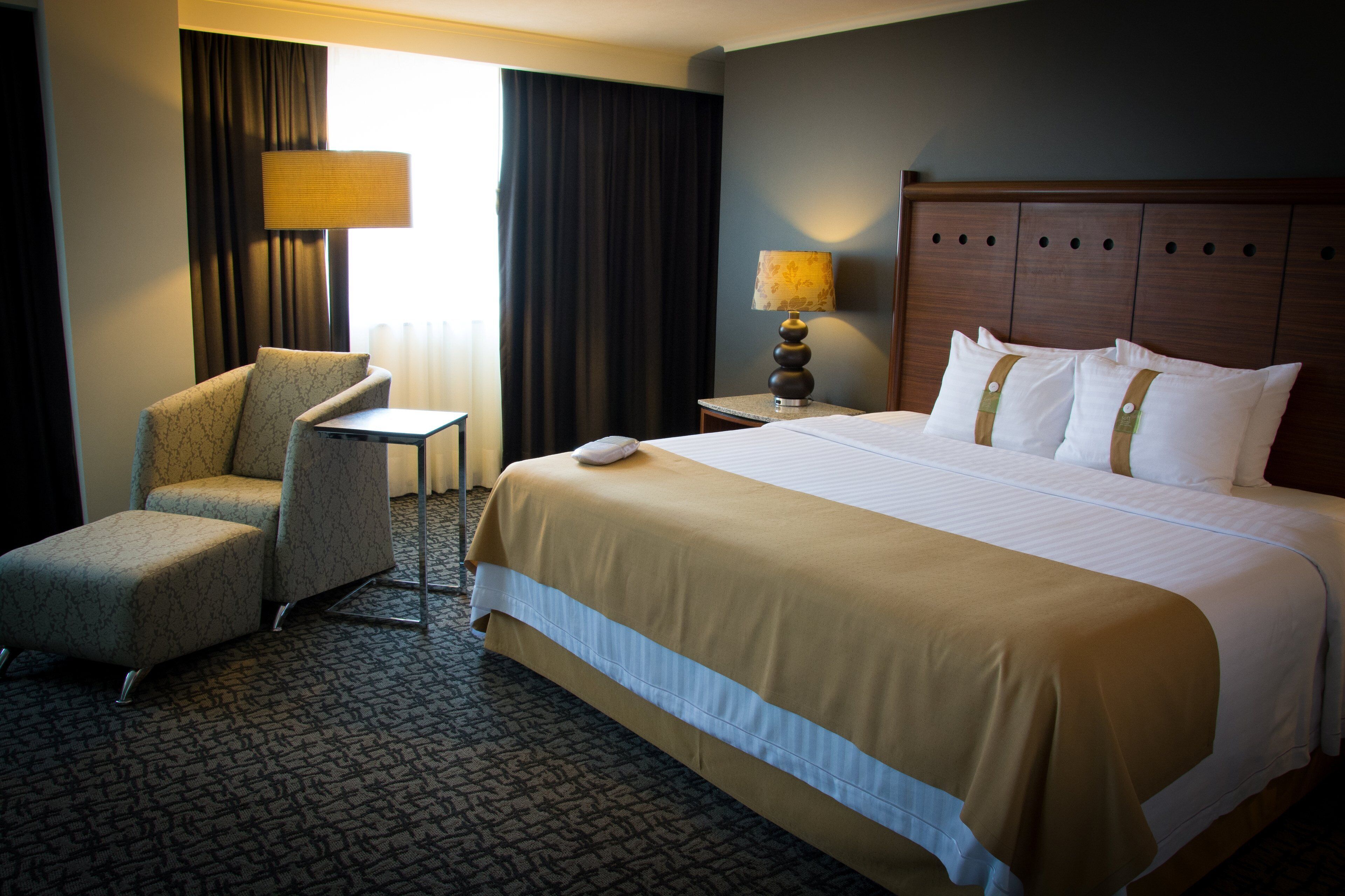 A hotel room with a large bed, a chair, a nightstand, and a lamp.