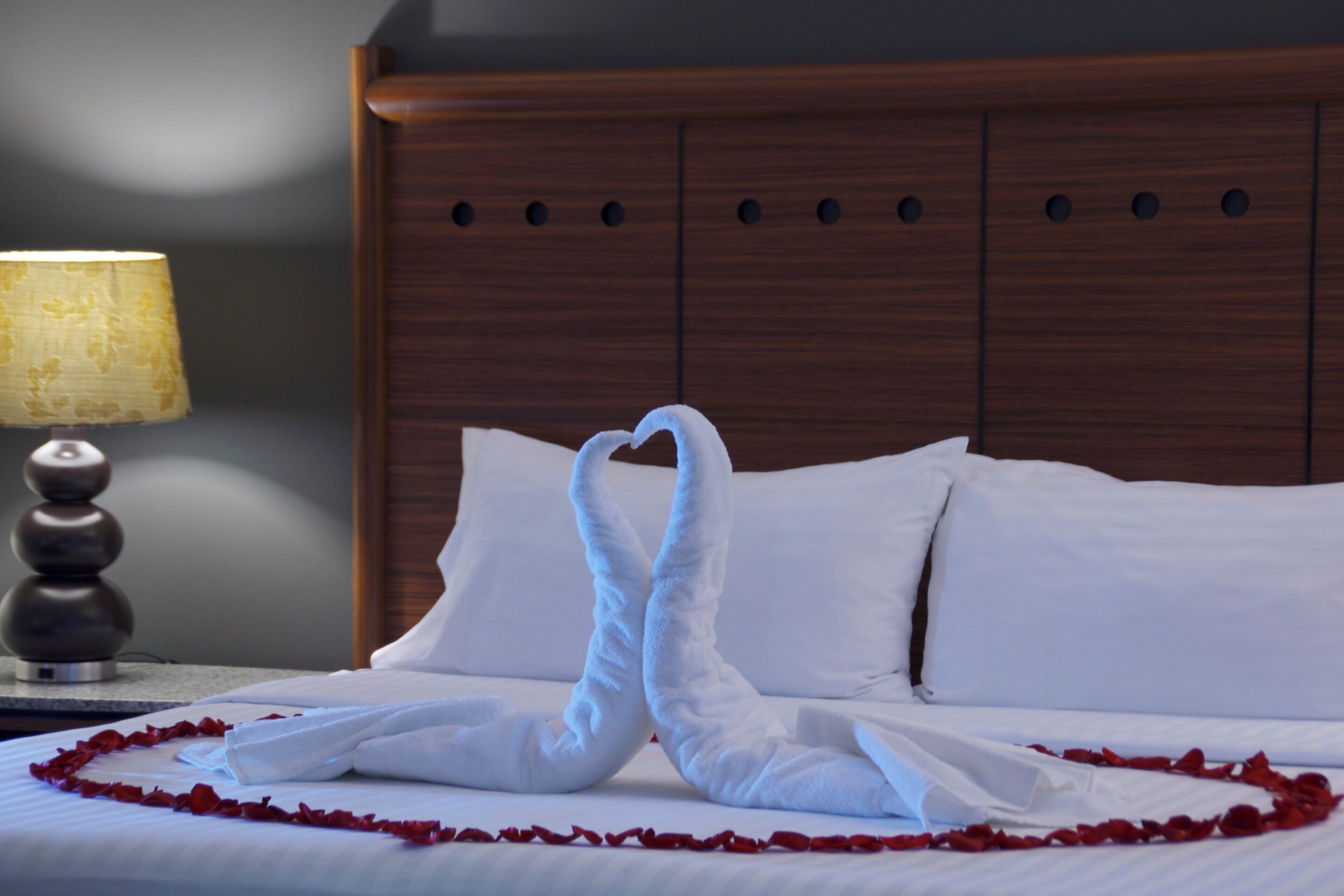 A bed with white linens, a wooden headboard, and a decorative swan made of towels.