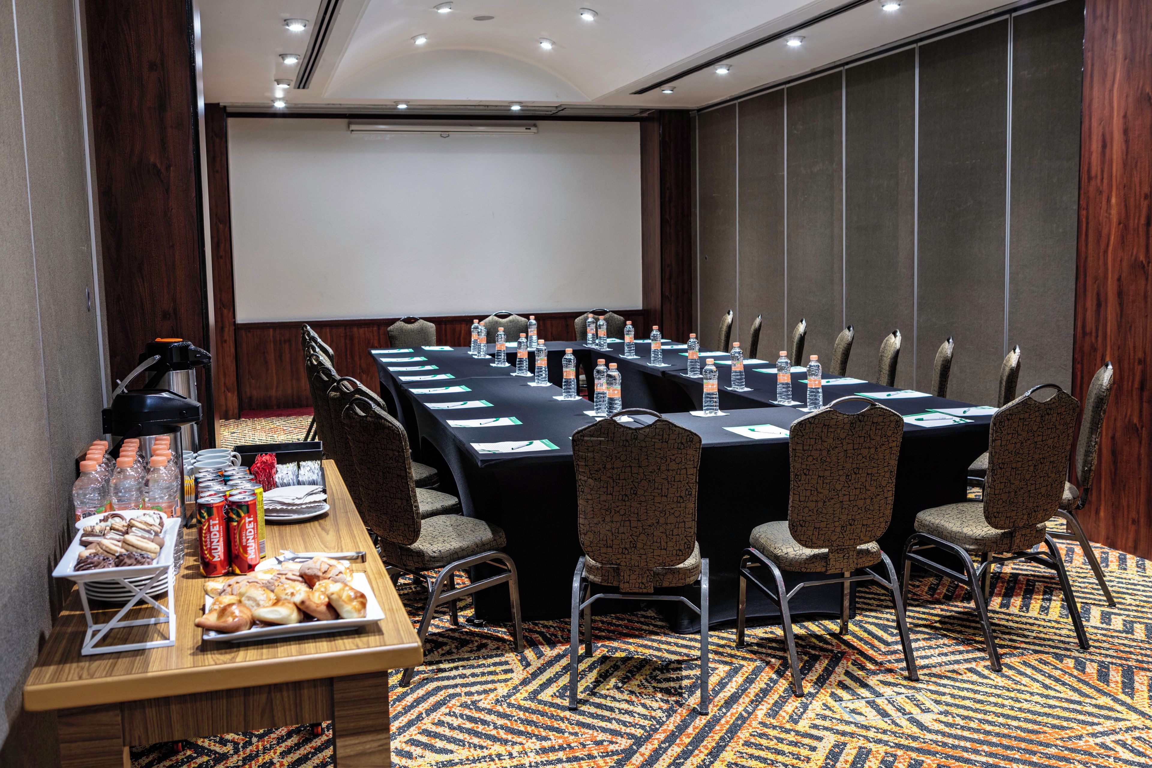 Une salle de conférence équipée d’une longue table, de chaises, d’un écran de projection et d’une table de buffet où sont disposés des collations et des boissons.