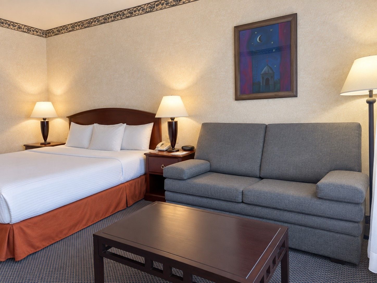 Ein Hotelzimmer mit Bett, Sofa, Nachttisch, Lampe und einem Gemälde an der Wand.