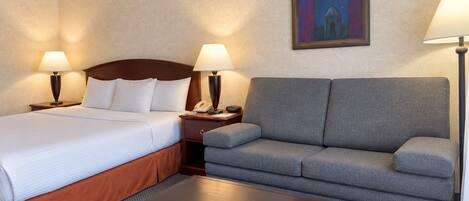Ein Hotelzimmer mit Bett, Sofa, Nachttisch, Lampe und einem Gemälde an der Wand.