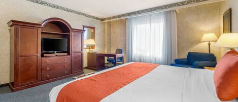 A hotel room with a large bed, a desk, a television, and a chair.