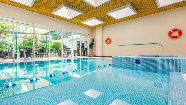 Una piscina interior con paredes de vidrio transparente, techo de baldosas y un flotador en la pared.