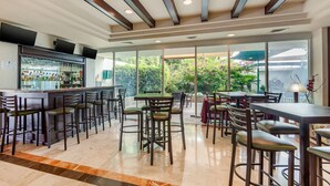 Un área de bar moderna con barra, varios taburetes y una zona de estar con mesas y sillas.