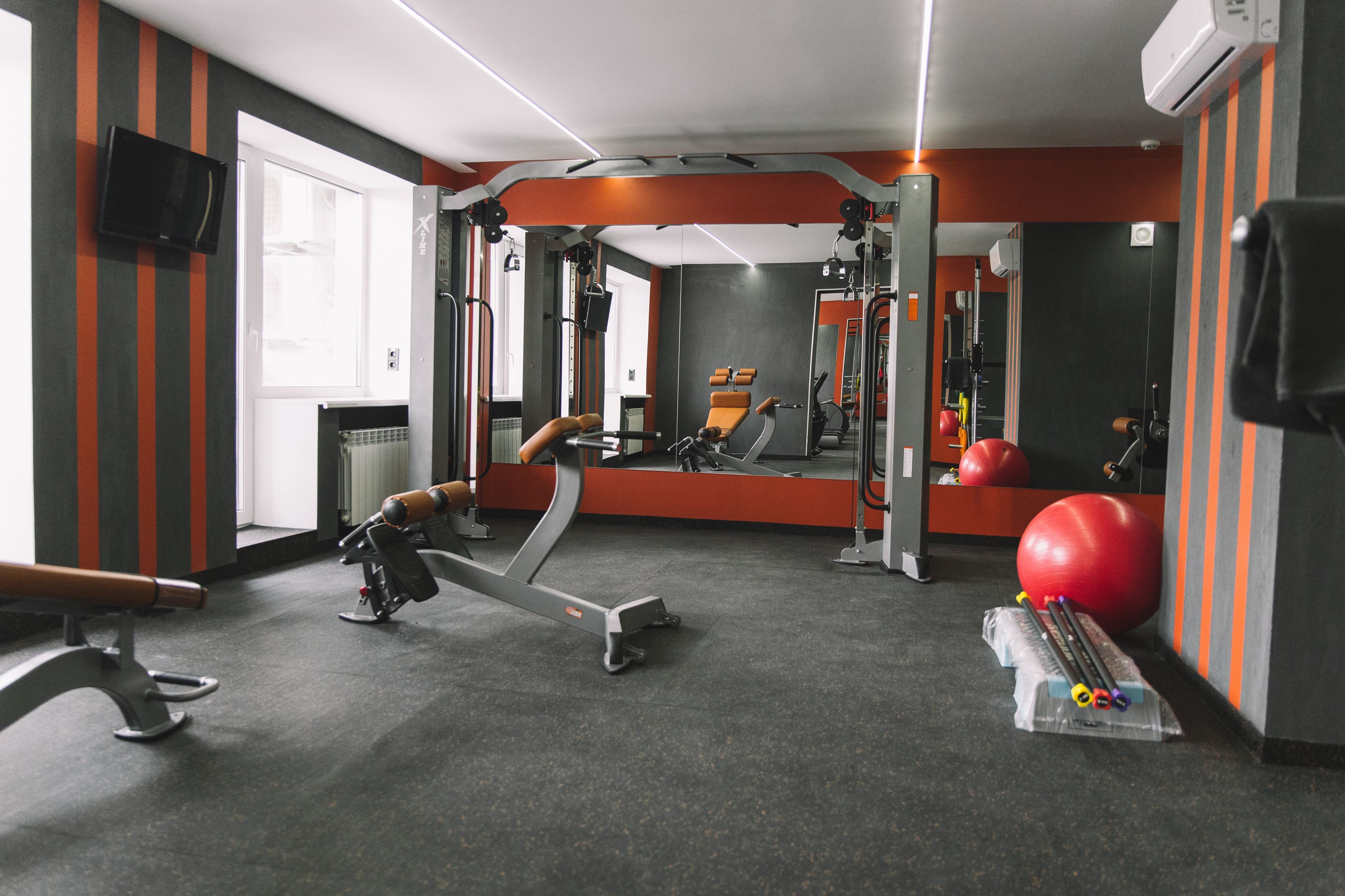Un gimnasio con equipo de ejercicio, un espejo y una pelota roja para hacer ejercicio.