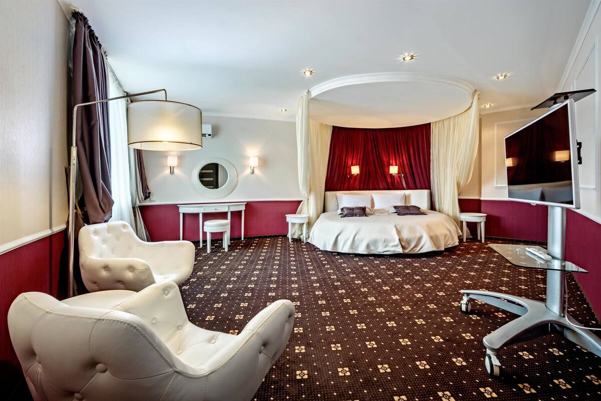 A hotel room with a large bed, a sitting area with a chair, a desk, and a TV.
