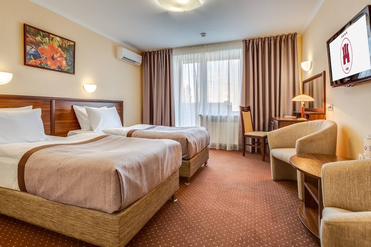A hotel room with two beds, a desk, a chair, and a TV.