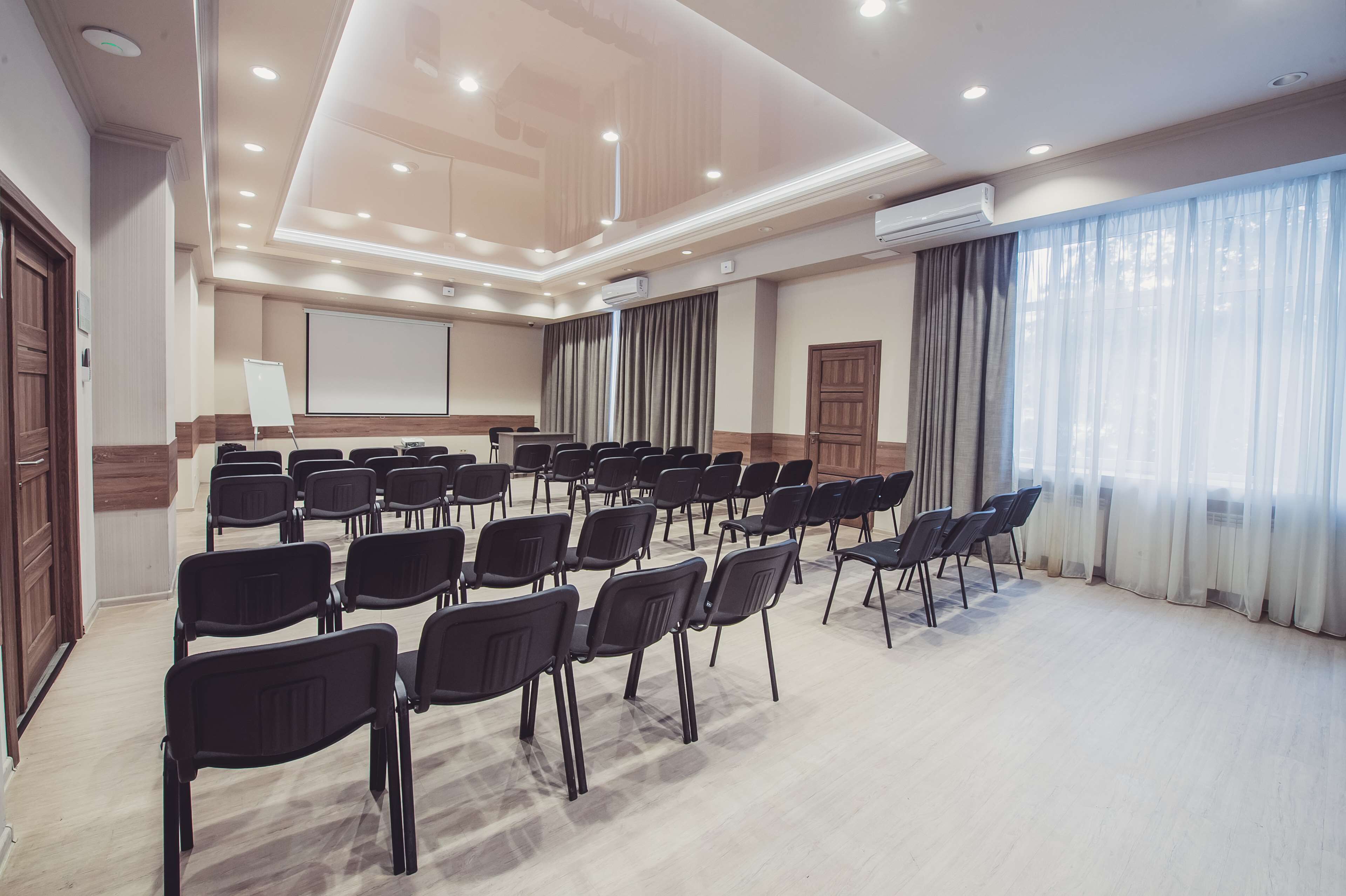 Ein Konferenzraum mit Reihen von Stühlen, einer Projektionsleinwand und einer Klimaanlage.