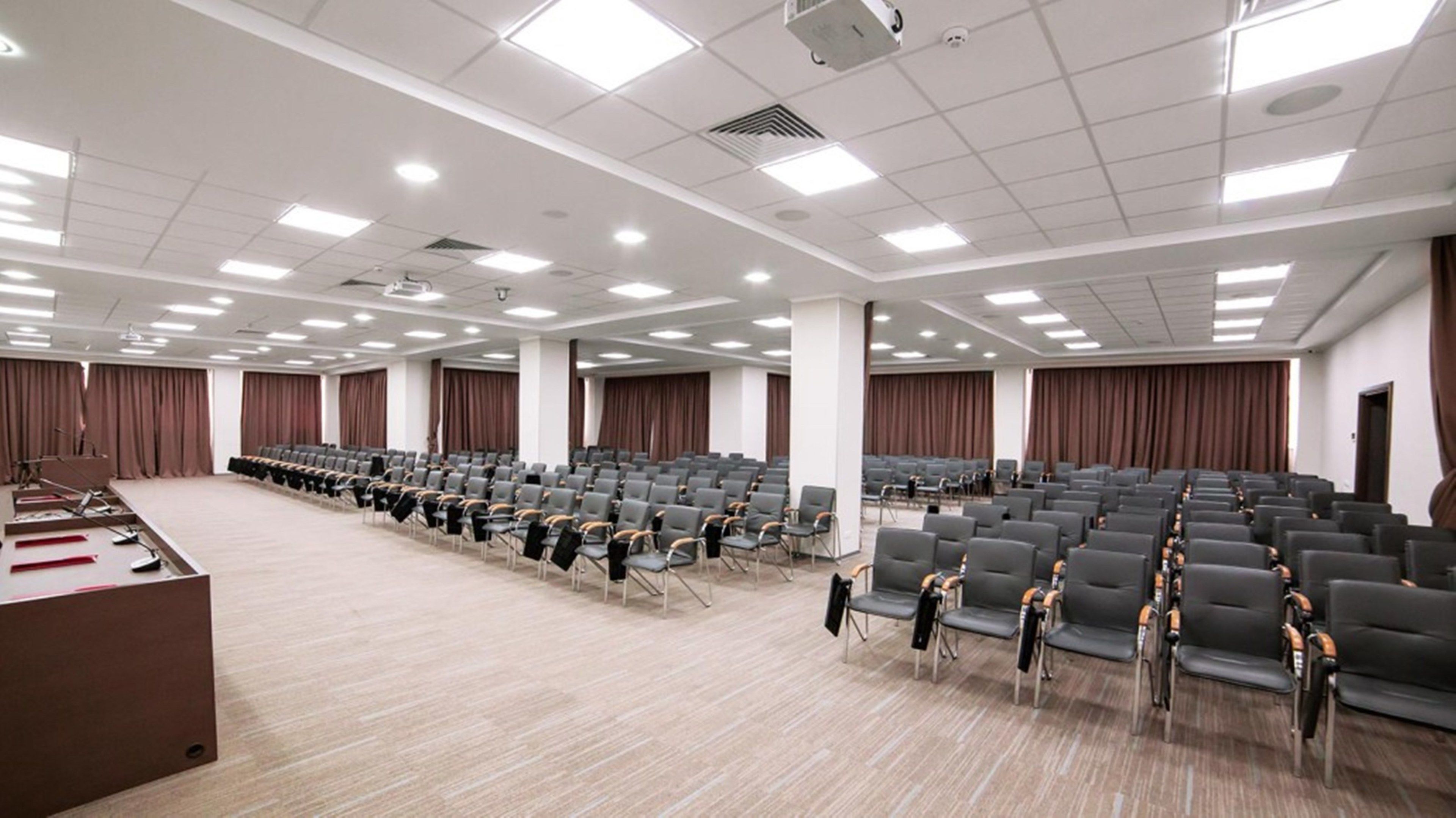 A large conference room with rows of chairs, a podium, and curtains.