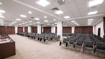 A large conference room with rows of chairs, a podium, and curtains.