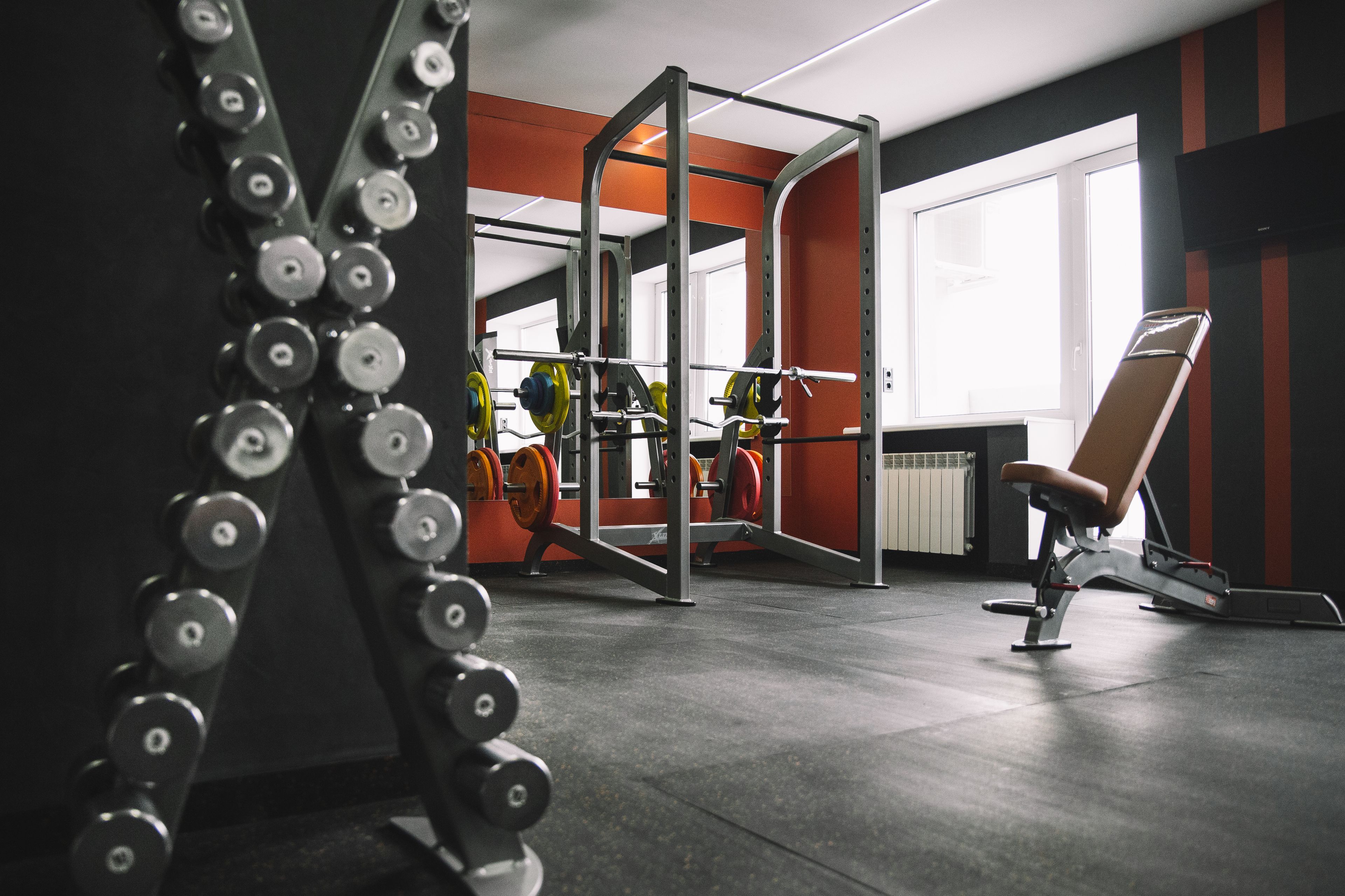 Un gimnasio con equipamiento de levantamiento de pesas, una jaula para sentadillas y una banca.