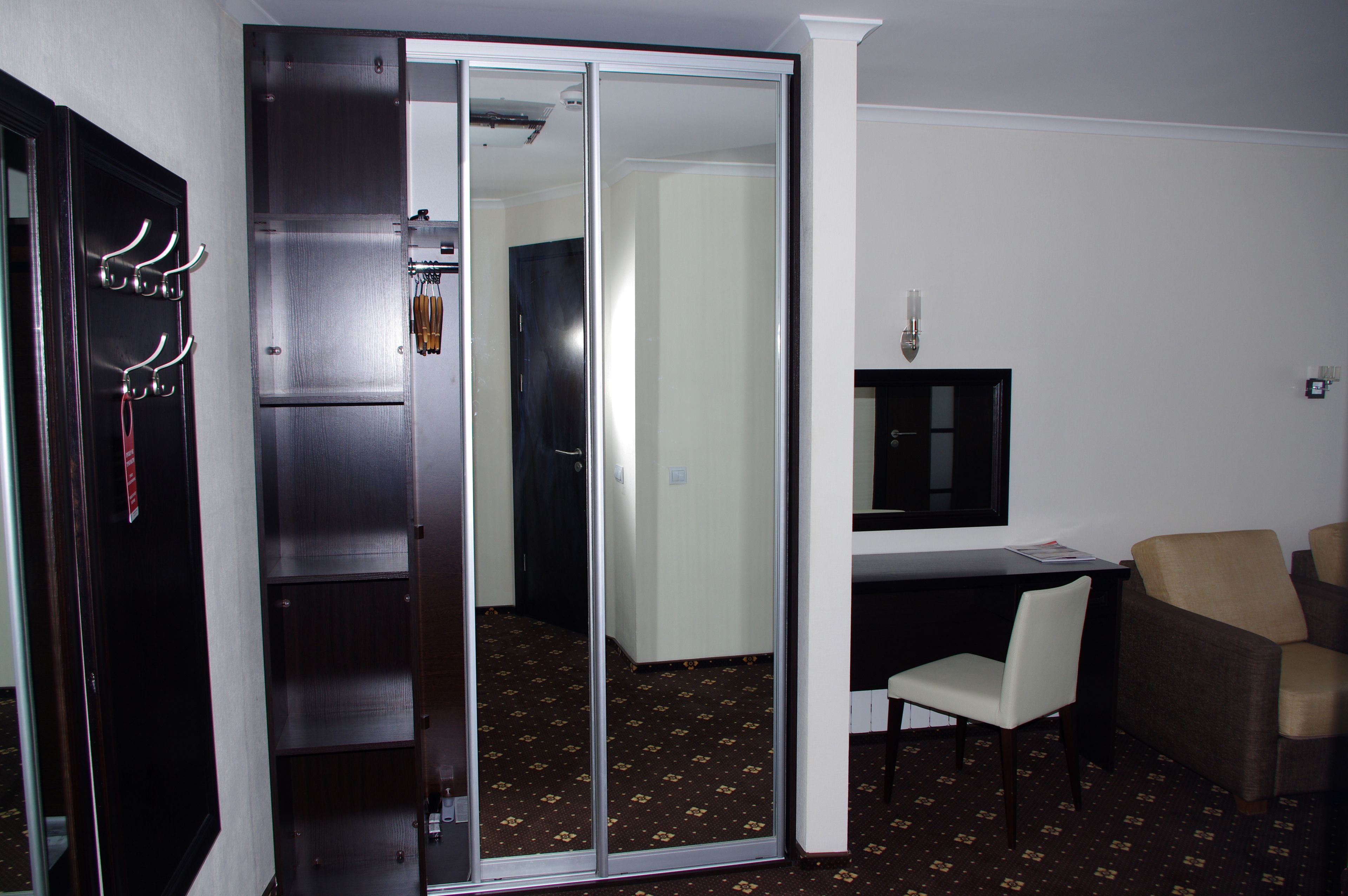 A hotel room with a sliding door closet, a desk with a chair, and a television.