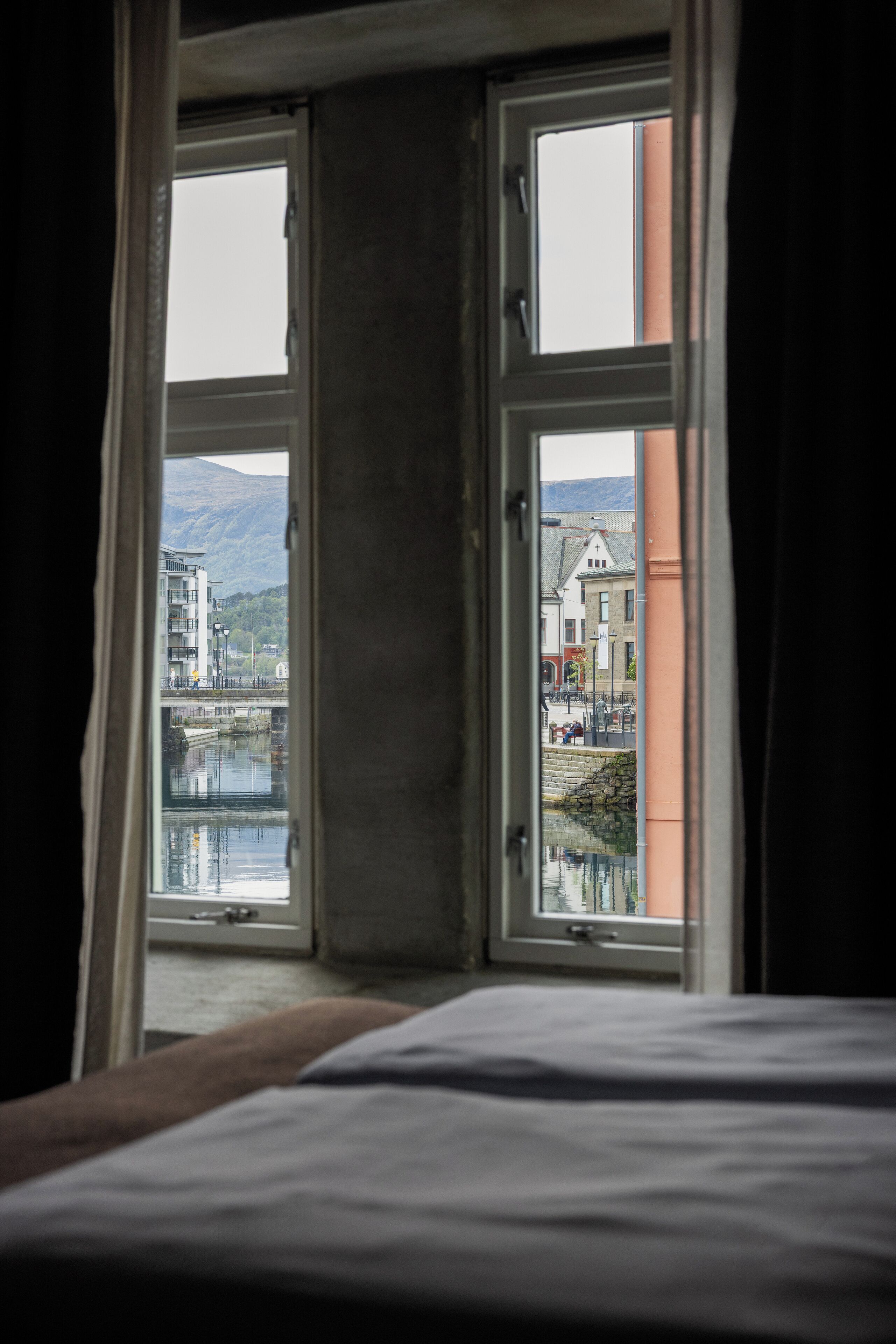 A room with a bed and a window overlooking a body of water and buildings.