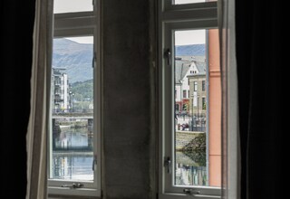 A room with a bed and a window overlooking a body of water and buildings.