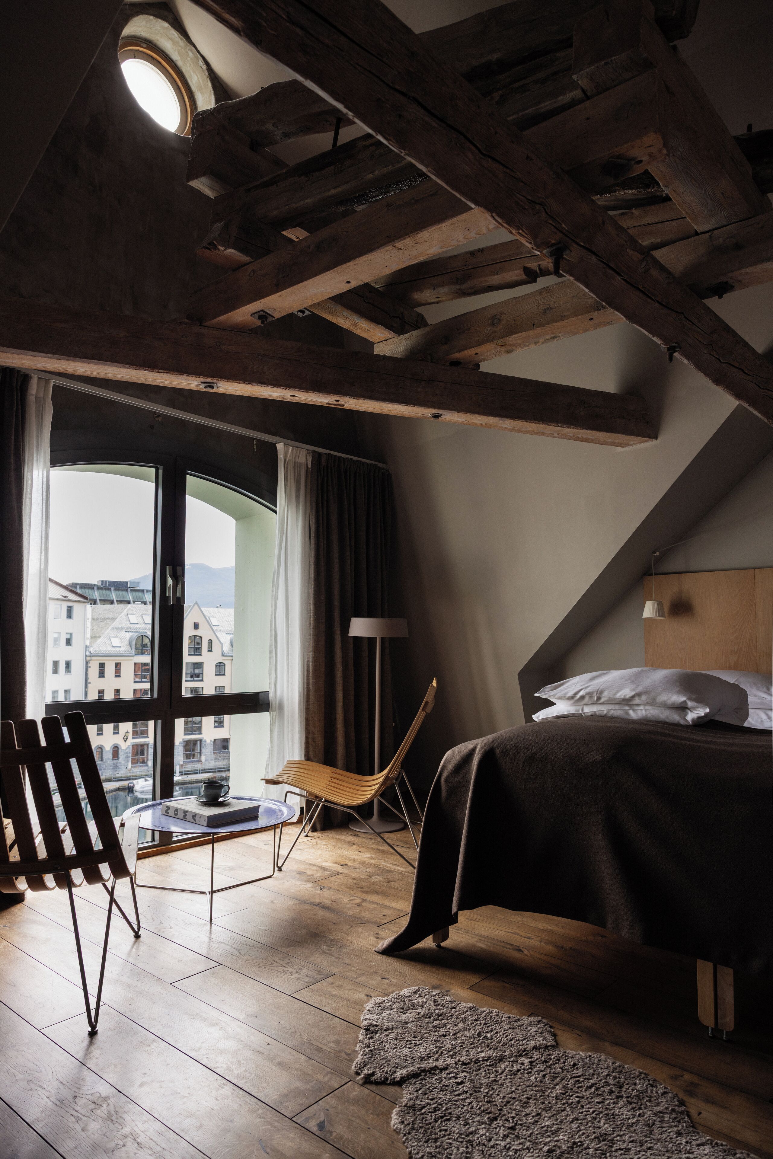 Un dormitorio con un ventanal grande, una cama, una silla y una mesita.