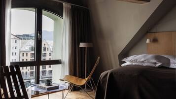 Un dormitorio con un ventanal grande, una cama, una silla y una mesita.