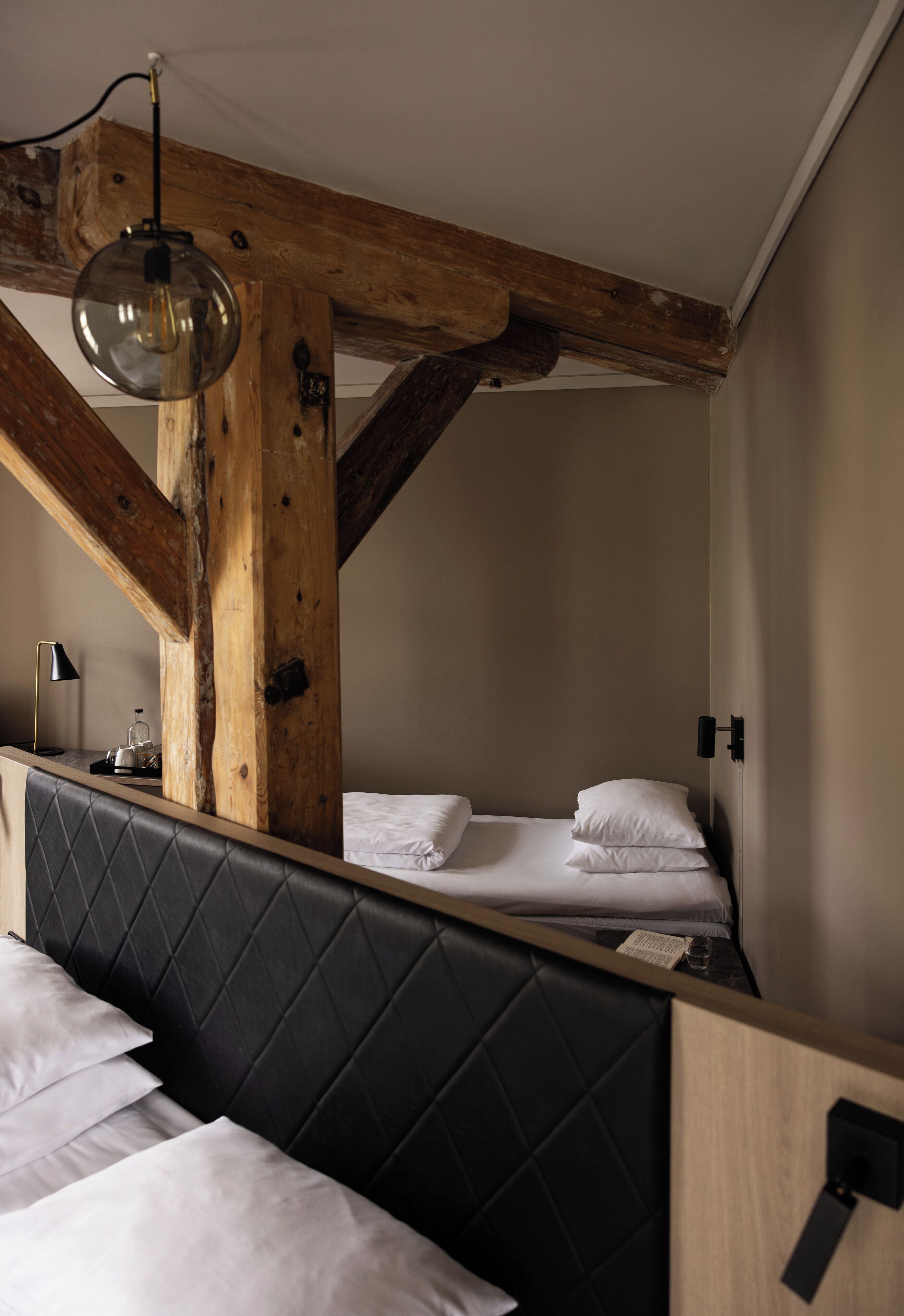 A room with a bed, a nightstand, a lamp, and exposed wooden beams.