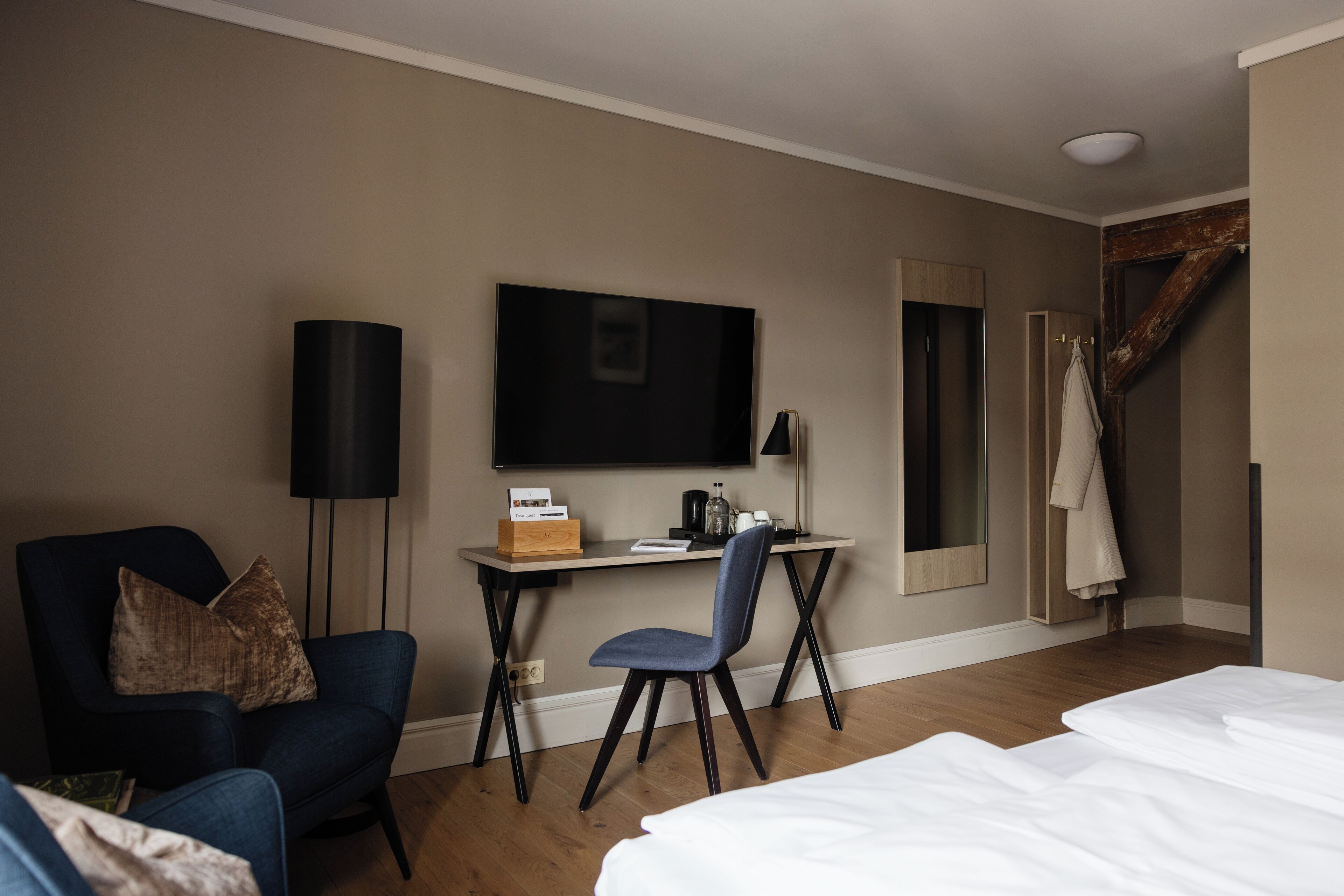 A hotel room with a bed, a desk with a chair, a TV, and a coat rack.