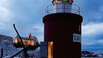 A lighthouse with a sign reading "SAKTT" at its base, surrounded by buildings and a body of water.