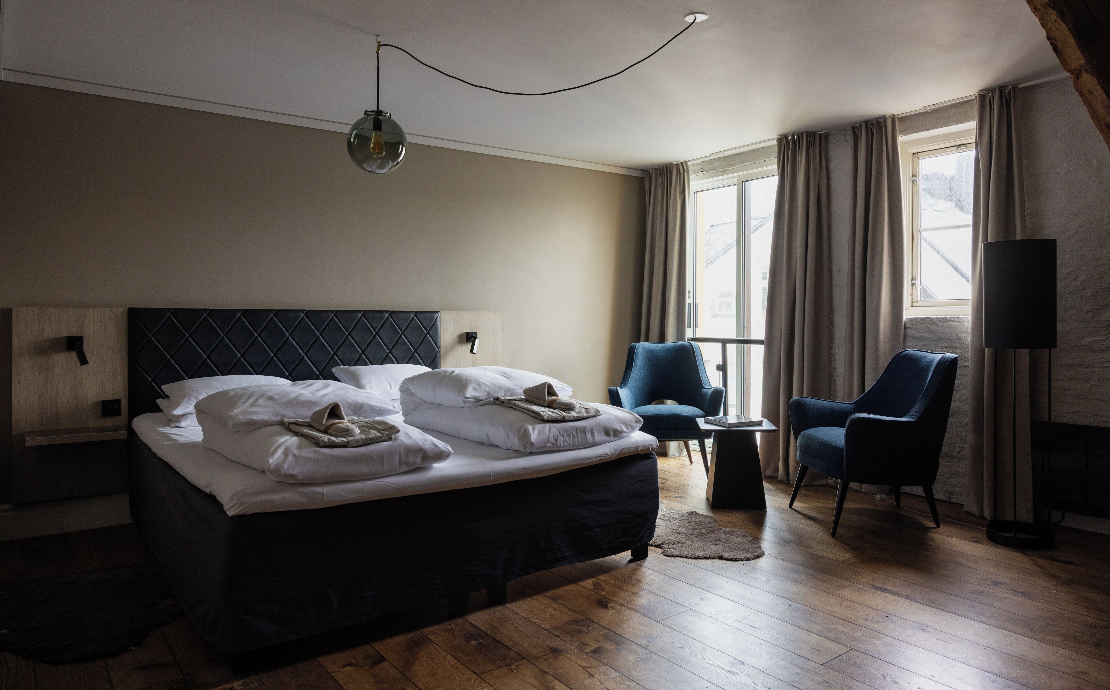 A hotel room with a large bed, two chairs, a small table, and a window with curtains.