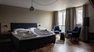 A hotel room with a large bed, two chairs, a small table, and a window with curtains.