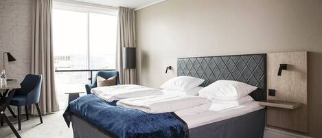 A modern hotel room with a large bed, a desk, and a chair.