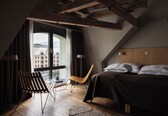 A modern hotel room with a large window, a bed, a chair, and a small table.