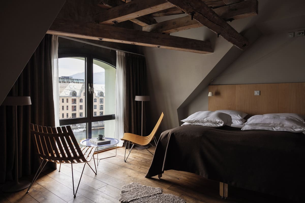 Ein modernes Hotelzimmer mit großem Fenster, einem Bett, einem Sessel und einem kleinen Tisch.